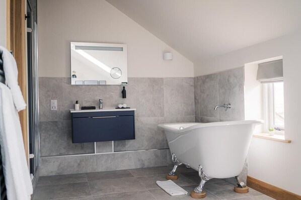 Un baño moderno con una bañera independiente, un tocador oscuro y un espejo grande.
