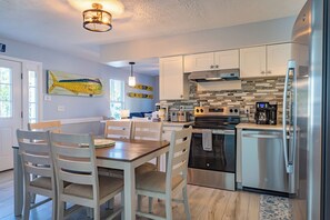 Una cocina moderna con armarios blancos, electrodomésticos de acero inoxidable y un comedor con sillas y mesa de madera.