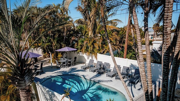 A swimming pool surrounded by palm trees and lounge chairs. - TranquiliSea 2: Pet friendly, long term discount, shared resort-style pool! (Holmes Beach)