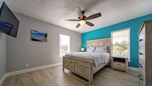A bedroom with a bed, a ceiling fan, a nightstand, a dresser, and a window. - TranquiliSea 2: Pet friendly, long term discount, shared resort-style pool! (Holmes Beach)