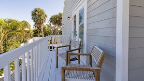 A wooden deck with white railings, two wooden chairs, and a white building with windows and a door. - TranquiliSea 2: Pet friendly, long term discount, shared resort-style pool! (Holmes Beach)