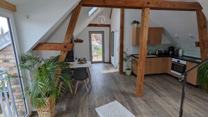 Een moderne loft met zichtbare houten balken, een keuken met een zwart aanrecht en een eethoek met een ronde tafel en stoelen.