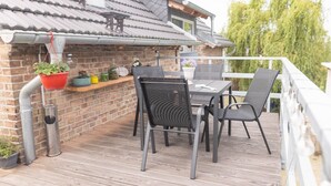 Een houten terras met een tafel, stoelen, een bakstenen muur en een hangplanter.