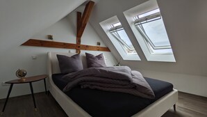 Een slaapkamer met een bed, een klein tafeltje, een wereldbol en dakramen.