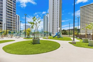 Un parc urbain moderne, doté de pelouses verdoyantes, d’aires de jeux et de grands immeubles résidentiels.
