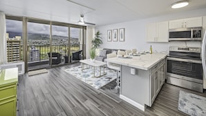A modern kitchen with a large island, stainless steel appliances, and a view of a cityscape through large windows. - City-Golf Course View Condo at the Waikiki Banyan w/Free Parking & WiFi (Honolulu)