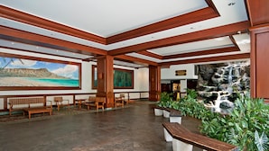 A lobby with wooden benches, a large painting of a beach, and a waterfall display. - City-Golf Course View Condo at the Waikiki Banyan w/Free Parking & WiFi (Honolulu)