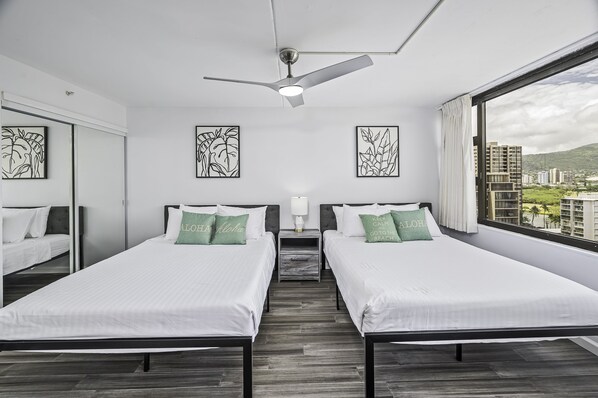 A modern hotel room with two single beds, a ceiling fan, and a large window offering a city view. - City-Golf Course View Condo at the Waikiki Banyan w/Free Parking & WiFi (Honolulu)