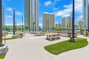 An outdoor patio area with tables and chairs, surrounded by tall buildings. - City-Golf Course View Condo at the Waikiki Banyan w/Free Parking & WiFi (Honolulu)