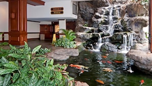 A hotel lobby with a koi pond, a waterfall, and a sign indicating 'Tower 1 Makai'. - City-Golf Course View Condo at the Waikiki Banyan w/Free Parking & WiFi (Honolulu)