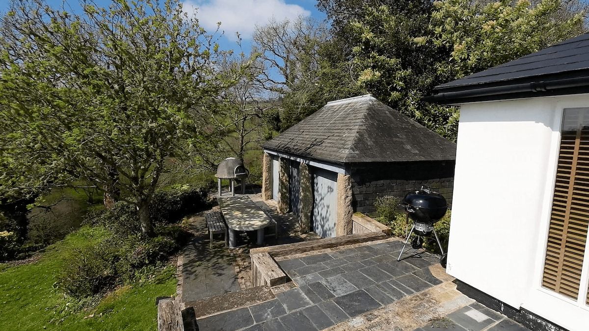 Une terrasse avec des sièges extérieurs, un barbecue et une petite construction dotée d’un toit à deux versants.