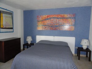 A bedroom with a bed, two bedside tables, a dresser, and a colorful abstract painting on the wall.