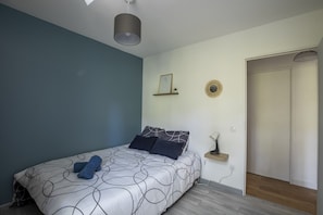 Quarto com cama, mesa de cabeceira, prateleira na parede e uma porta.