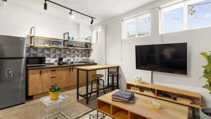 A modern kitchen with a built-in oven, microwave, and coffee machine. There is a dining area with a table and chairs, and a TV mounted on the wall. - MS Moderna Suite Arcos Hercules (Santiago de Querétaro)