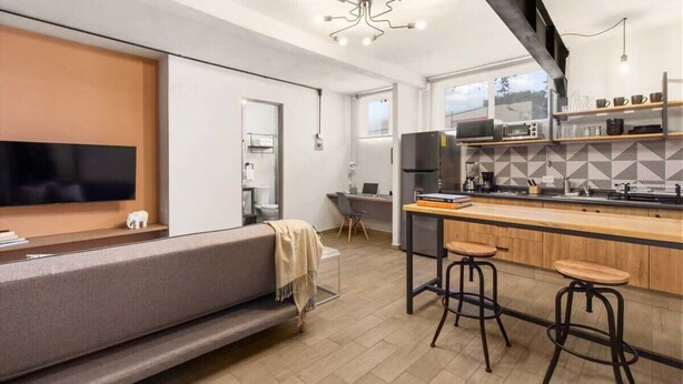 Una cocina moderna con horno empotrado, una zona de comedor con un taburete de bar y un televisor de pantalla plana grande.