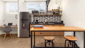 Una cocina moderna con una mesa de madera, dos taburetes, un refrigerador, un microondas y una cafetera.
