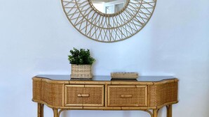 A rattan console table with two drawers, a woven mirror above it, and a small potted plant on the table.