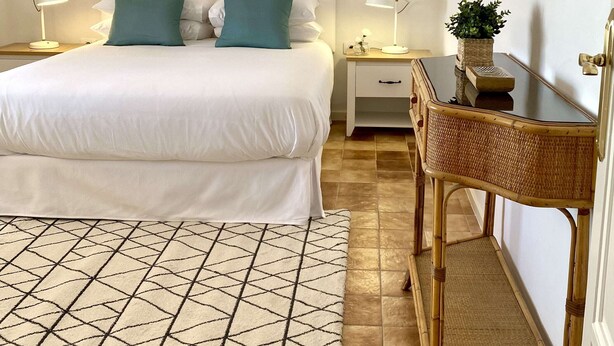 A neatly arranged bedroom with a bed, bedside tables, a desk, and a hanging macrame decoration.