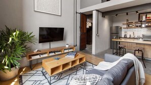 Un soggiorno moderno con una televisione a schermo piatto, un tavolino in legno, un divano grigio e un'ampia pianta in vaso.