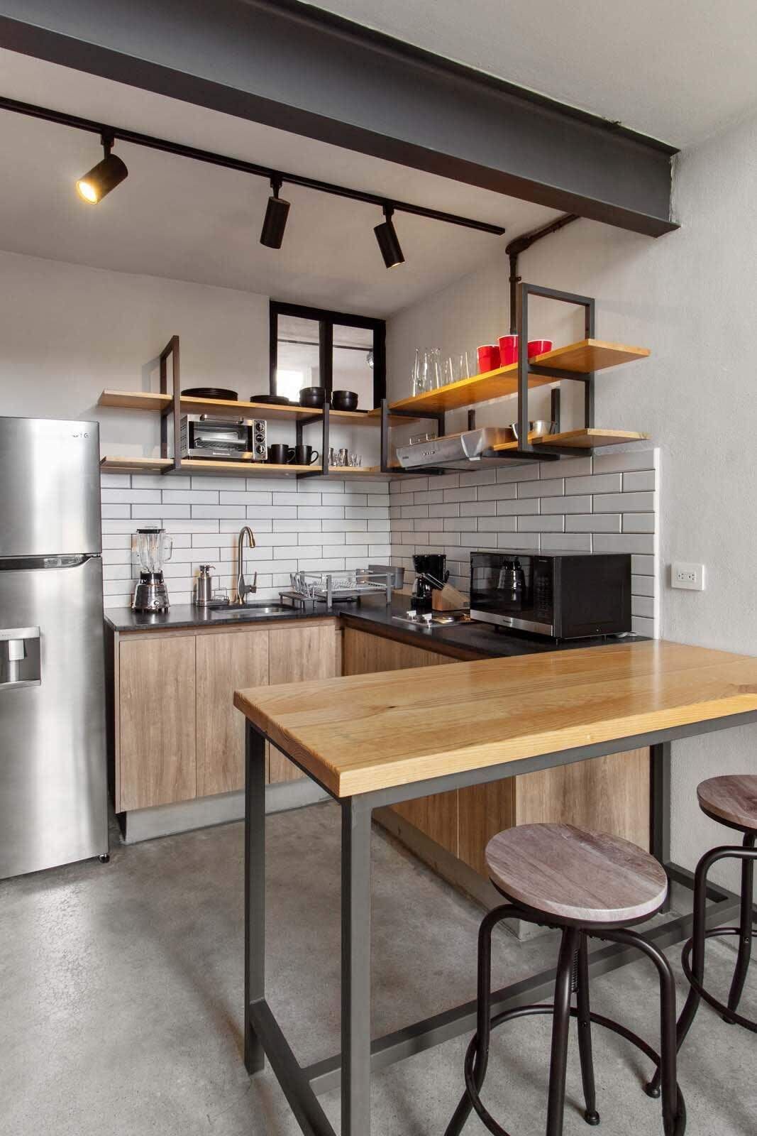 A modern kitchen with a wooden table, bar stools, a built-in oven, and a microwave.