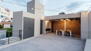 Un'area patio esterna moderna con un tavolo e sedie da pranzo, un muro in mattoni e luci a stringa.