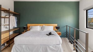 A modern bedroom with a large bed, wooden shelving, a nightstand, and a window with a view. - +MS +Cómoda Suite +Hércules (Santiago de Querétaro)