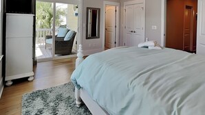 A bedroom with a large bed, a ceiling fan, a sliding glass door to a balcony, and a white wardrobe. - Serenity by the Sea | Community Pool + Near Beach! (Kure Beach)