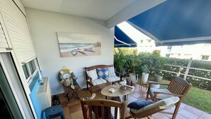 Un patio con una mesa y sillas de madera, un banco y un cuadro de barcos en la pared.