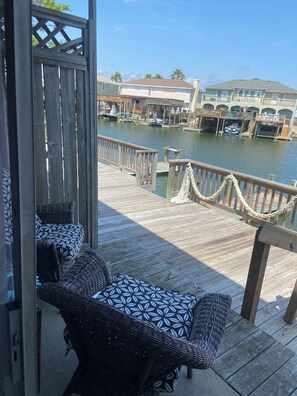A wooden deck with wicker furniture overlooking a marina with boats and buildings. - Cozy Condo on the Canal (Corpus Christi)