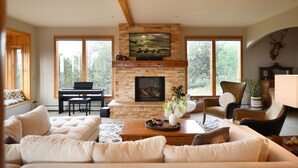 Una sala de estar con chimenea, un piano y un ventanal grande.