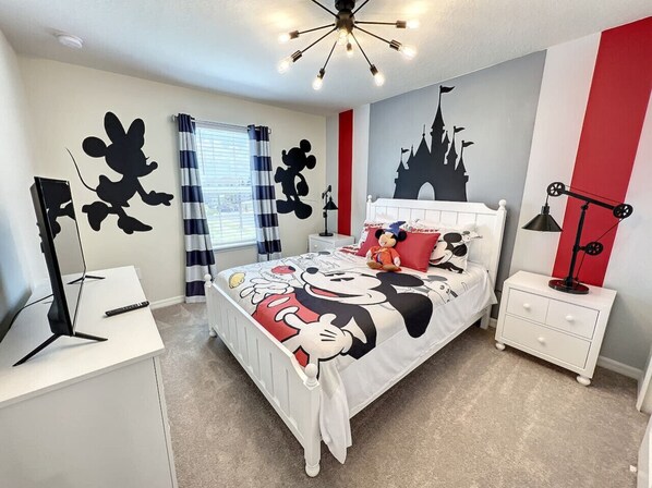 A bedroom with a Mickey Mouse themed bedspread, a white dresser, a nightstand, and a castle silhouette on the wall.