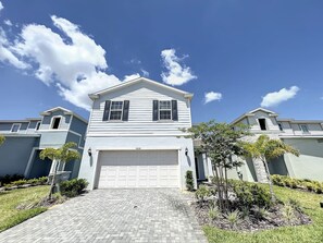 A two-story house with a garage, surrounded by a landscaped garden and a paved driveway.