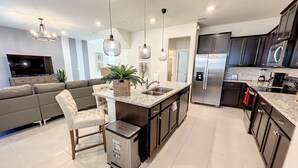 Une cuisine moderne dotée d’un îlot central, de meubles de couleur sombre, d’appareils électroménagers en acier inoxydable et de luminaires suspendus.