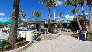 Un complexe hôtelier doté d’un espace extérieur aménagé avec des tables et des chaises, de palmiers et d’une piscine.