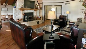 Una sala de estar acogedora con chimenea de piedra, sofás de cuero, televisor y comedor con mobiliario de madera.