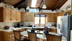 Una cocina con armarios de madera, un refrigerador, un microondas y un comedor con sillas.