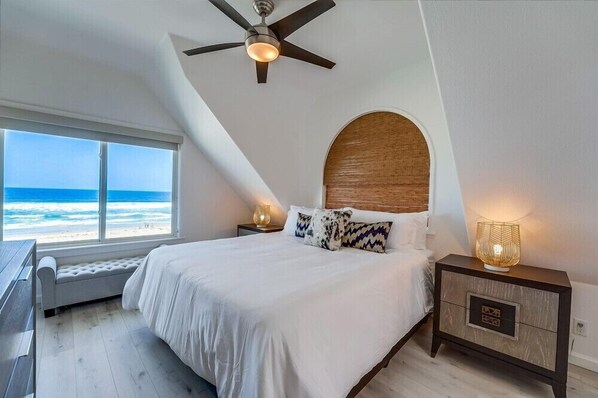 A bedroom with a large bed, a ceiling fan, a nightstand with a lamp, and a view of the ocean. - 2 Levels of Ocean Front + Exclusive Water View Deck (San Diego)