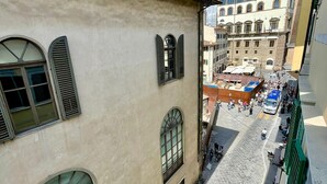 Eine enge Straße mit Häusern an beiden Seiten, ein Marktbereich mit Menschen und Ständen, und ein Turm im Hintergrund.