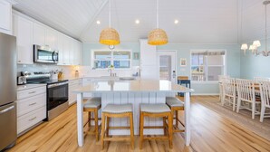 Une cuisine moderne avec des meubles blancs, des appareils en acier inoxydable, un îlot central doté de tabourets de bar et des suspensions en osier.