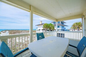 Un espace extérieur abrité, doté d’une table et de chaises, d’une rambarde blanche, et offrant une vue sur la plage et les bâtiments en arrière-plan.