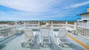 Une terrasse avec des chaises blanches et vue sur la plage.