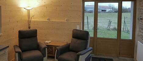 A room with two leather chairs, a small wooden table, a lamp, and a door leading outside.