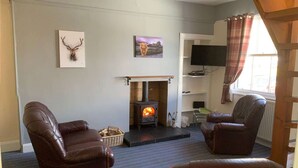 A living room with a fireplace, leather chairs, and artwork on the wall. - Cottage with Log Burner - Wanlockhead D & G (Wanlockhead)