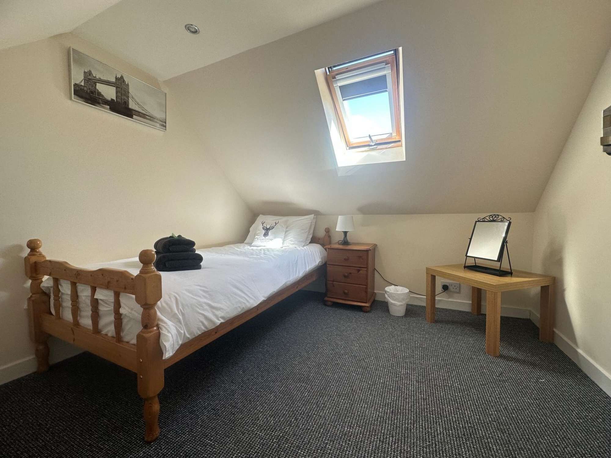 Una camera da letto con un letto singolo, un comodino, un tavolino con uno specchio, una finestra e un quadro raffigurante un ponte sulla parete.