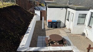 A residential area with a paved patio, a wooden table and benches, and three trash bins. - Cottage with Log Burner - Wanlockhead D & G (Wanlockhead)