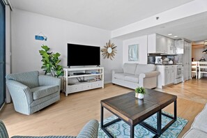 A living room with a sofa, a coffee table, a TV, and a kitchen in the background.