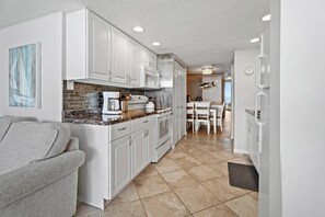 Une cuisine moderne avec des meubles blancs, un plan de travail en granit et un coin repas comprenant une table et des chaises blanches.