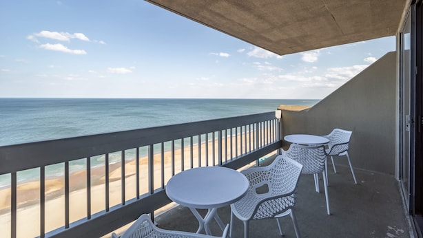 Un balcon donnant sur la plage, des chaises en métal blanc et un plafond en béton.