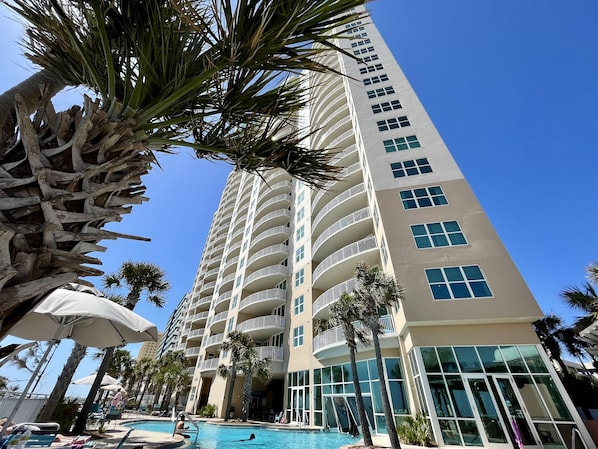 Un hôtel de grande hauteur doté de nombreux balcons, d’une piscine et de palmiers.