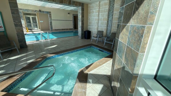 An indoor swimming pool with a separate hot tub area, tiled walls, and a seating area with chairs.
